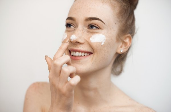 Junge Frau mit Gesichtscreme auf Nase und Wangen lacht. Kategoriebild Naturkosmetik - Gesichtscreme.